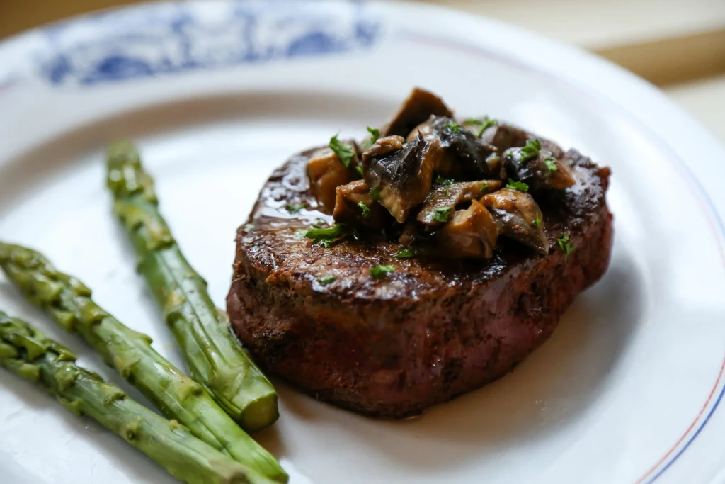 Seared steak with mushrooms, herbs, and asparagus on a decorative plate.