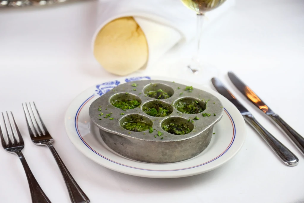 Escargots in metal dish with green butter, on a table setting.