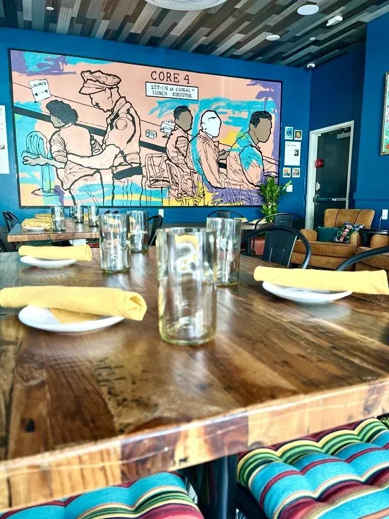 Restaurant interior with wooden table and mural: "SIT-IN at CANAL LUNCH COUNTER."