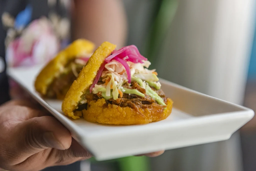 Two golden arepas with shredded meat, coleslaw, and pickled onions.