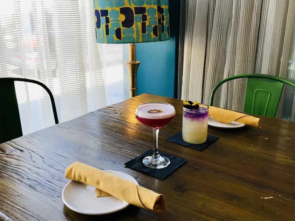Red and layered purple cocktails on a dark table, restaurant setting.