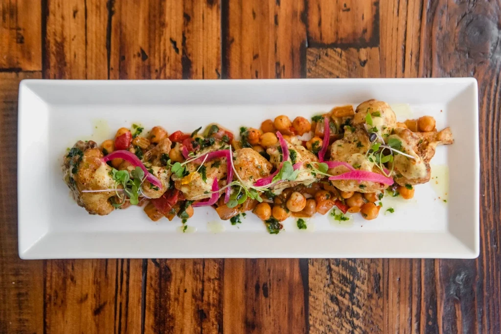 Pan-seared scallops with chickpeas, red vegetables, and microgreens on a white plate.