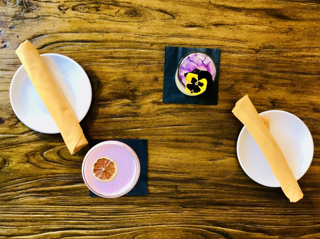 Two layered drinks/desserts with garnishes on a wooden table setting.