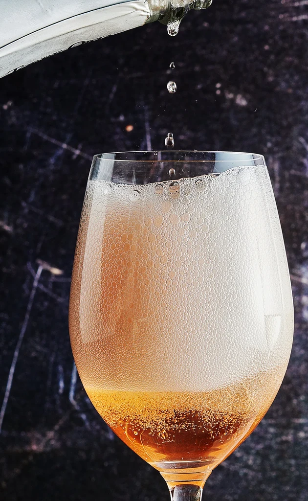 Clear wine glass filling with sparkling rosé, foam, and falling drops.