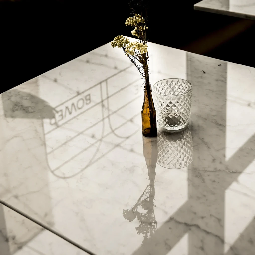 Marble table with flowers, glass tumbler, and "BOWER" reflection.