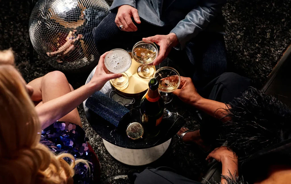Three people clinking drinks around a table with a disco ball.