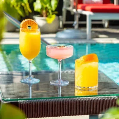 Three colorful cocktails on a table by a sparkling blue swimming pool.