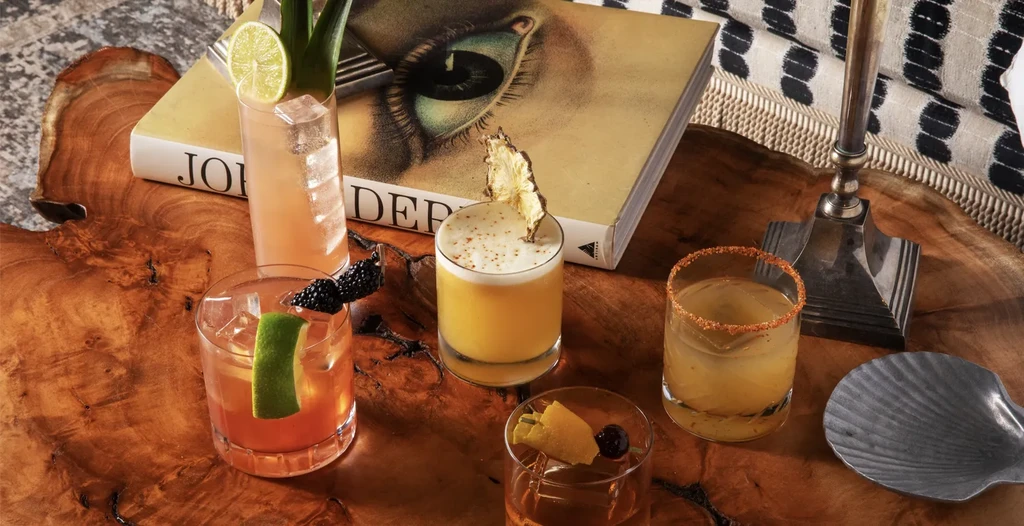 Flat lay of five uniquely garnished cocktails on a polished wooden table.