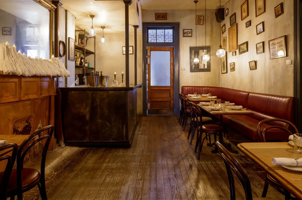 Dimly lit restaurant with red banquettes, set tables, and framed art.