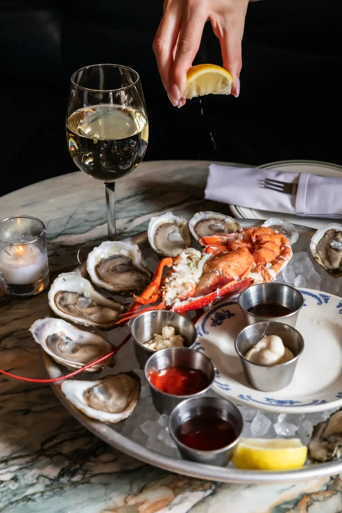 Hand squeezing lemon over oysters and lobster on a platter with sauces.