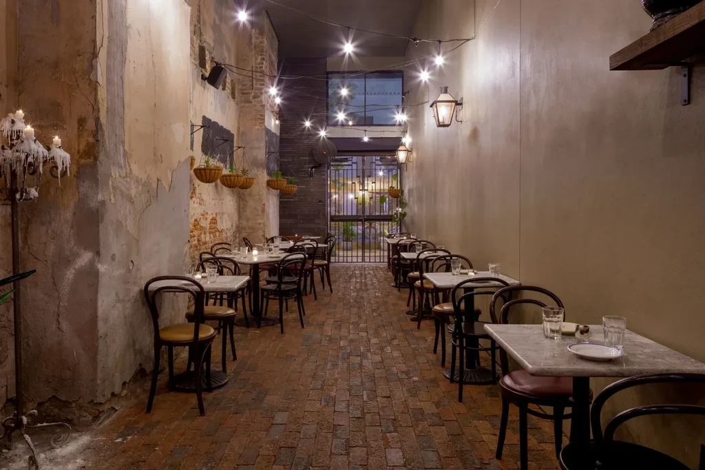 Rustic old-world alleyway restaurant dining area, dimly lit by string lights.