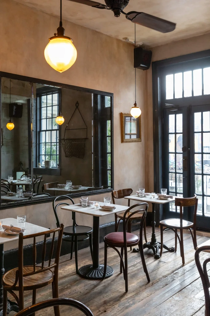A warm, rustic restaurant interior with marble tables and bentwood chairs.