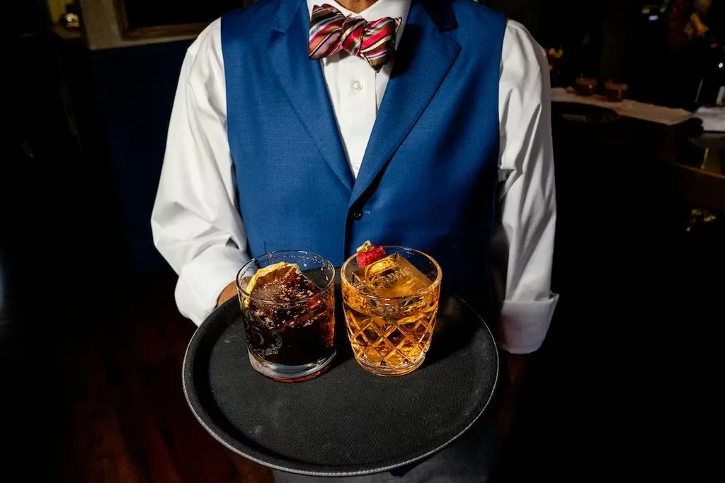 Server holding tray with dark and amber garnished cocktails.