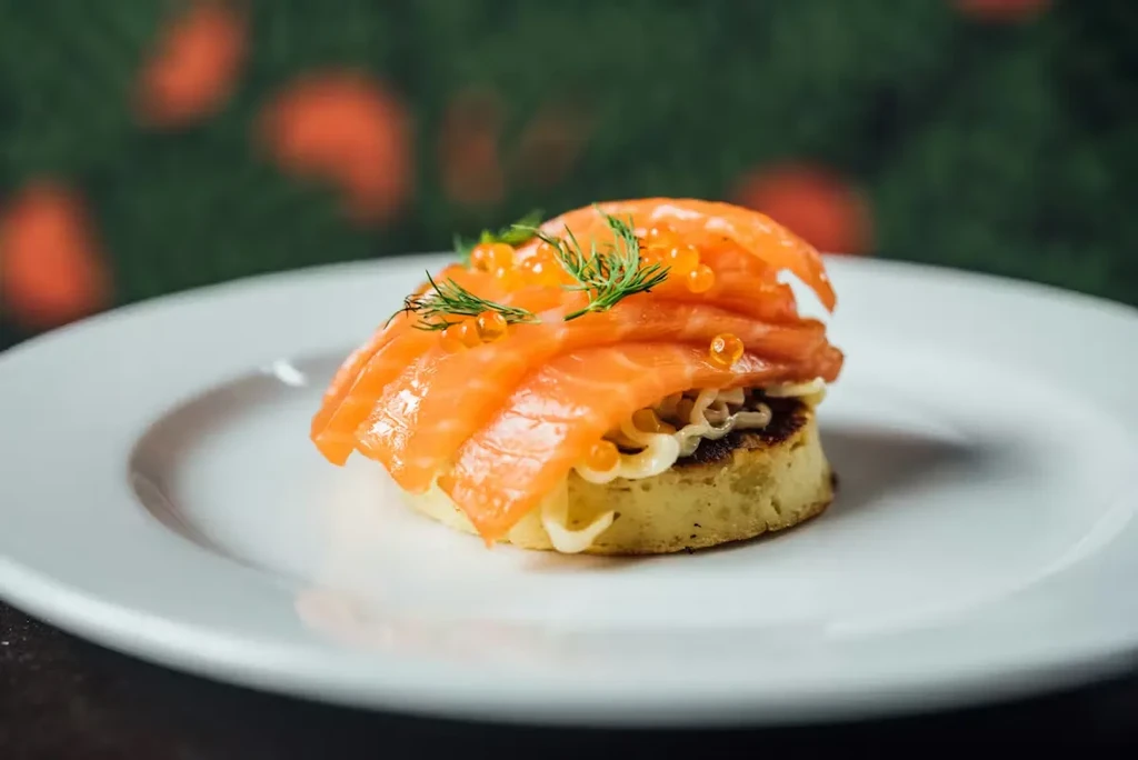 Golden blini with smoked salmon, salmon roe, and dill on white plate.