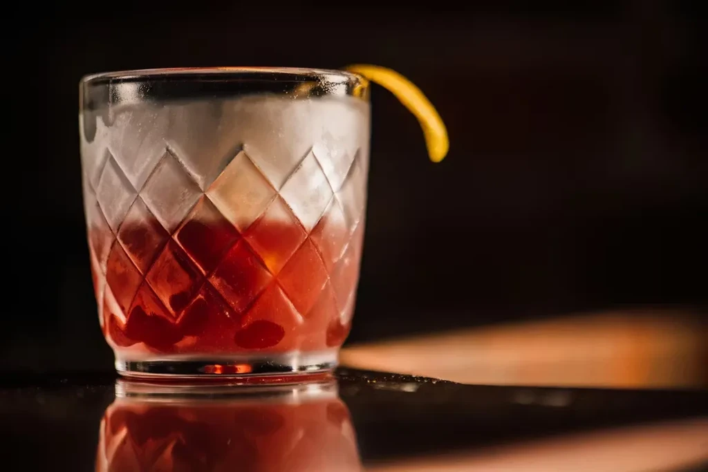 Foamy reddish-orange cocktail with citrus twist in a cut-glass tumbler.