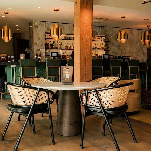 Modern restaurant interior with marble table, cane chairs, and stocked bar.