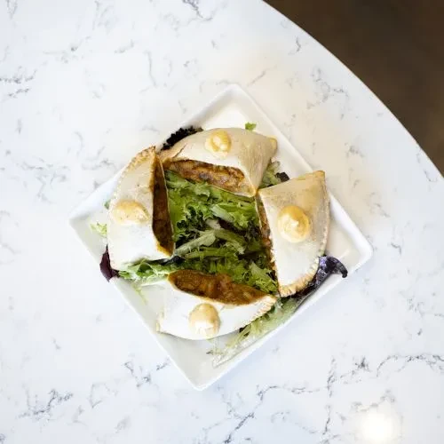 Four savory pastries, halved, with sauce and salad on a white plate.