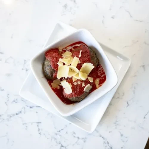 Meatballs in red sauce with Parmesan in a square white bowl.