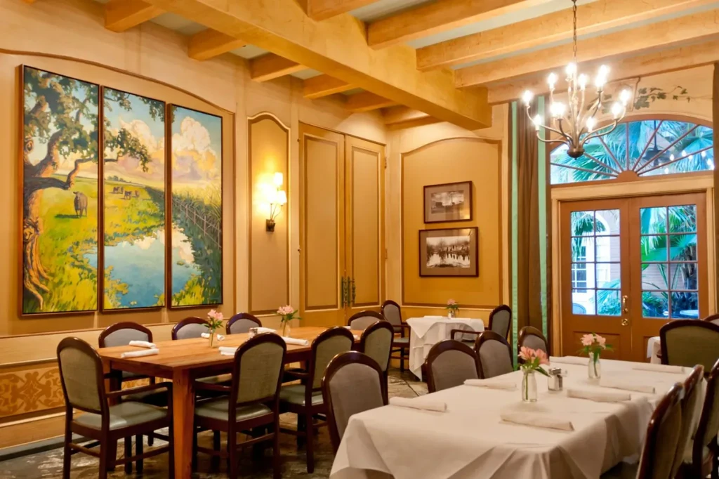 Elegant restaurant interior with yellow walls, landscape art, and set tables.