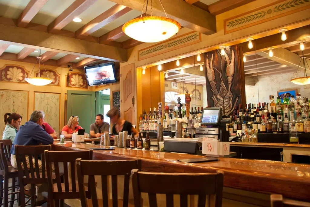 Lively bar interior with patrons, bartender, wooden counter, and lobster mural.