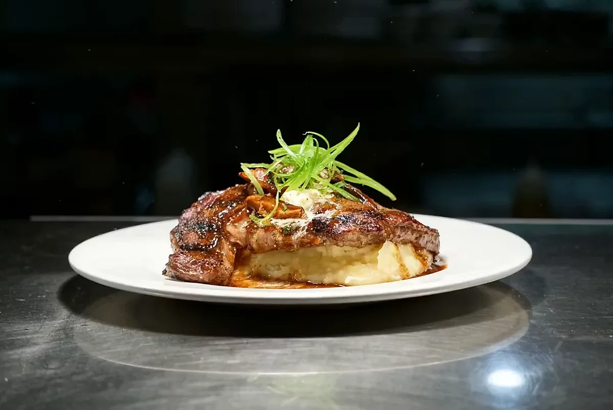 Grilled steak over mashed potatoes topped with scallions on white plate