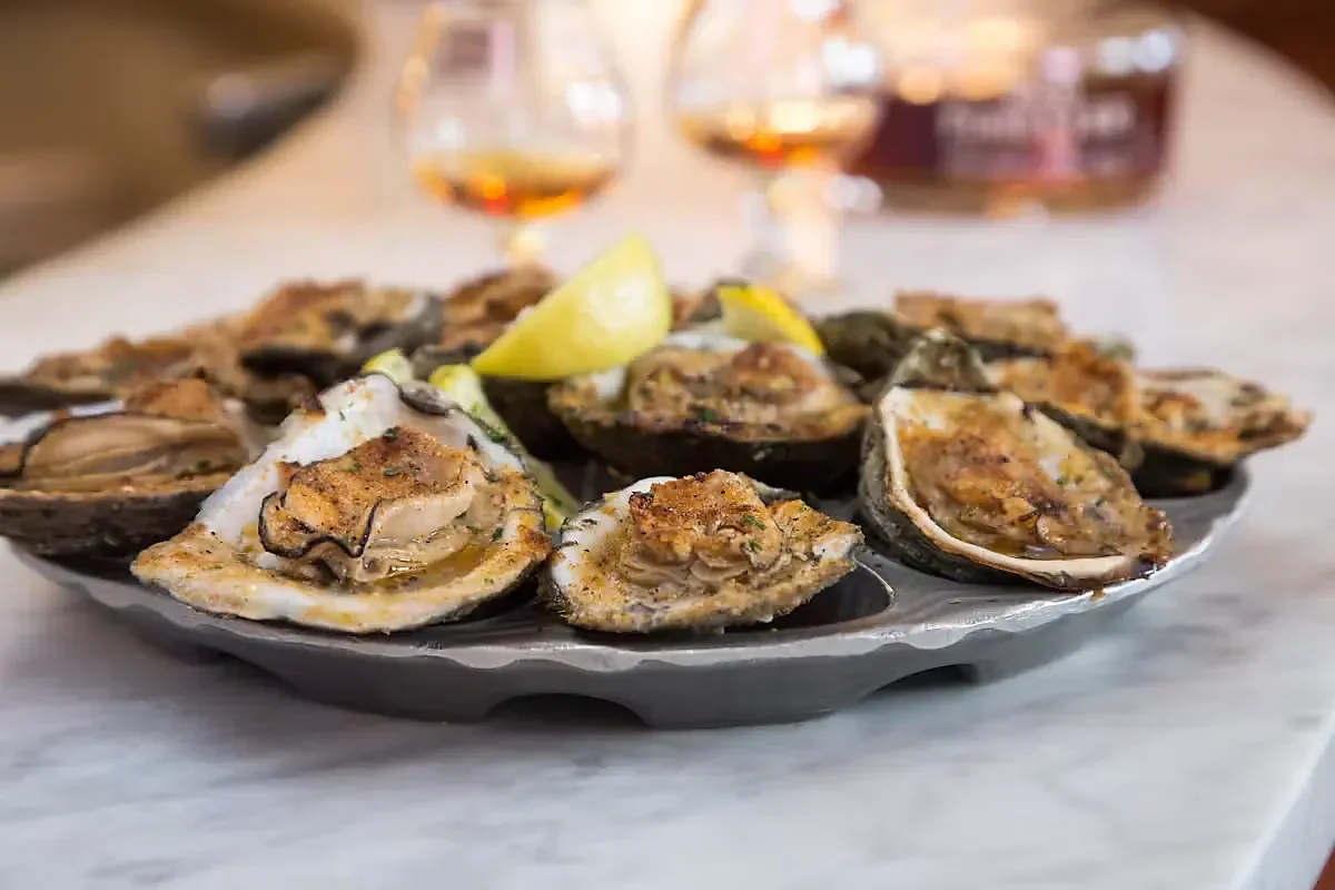 Charbroiled oysters on a platter with lemon and whiskey glasses