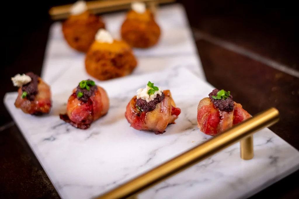 Savory bacon-wrapped bites, croquettes with cream on marble board.