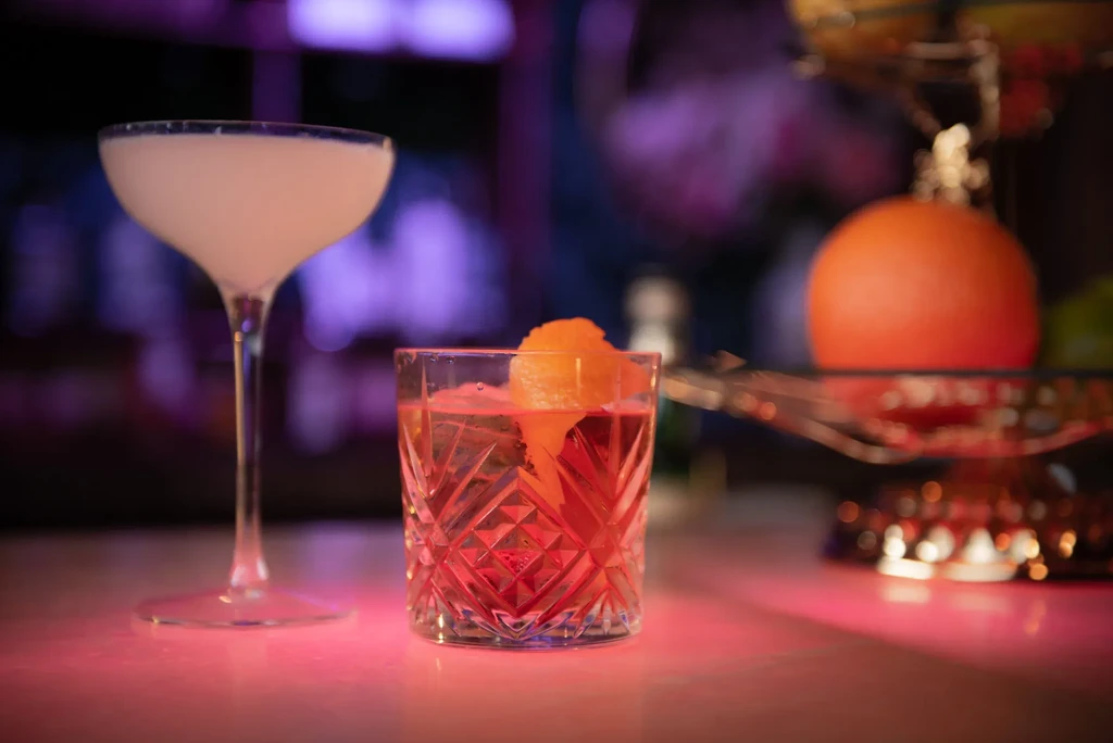 White coupe and red rocks cocktails on a glowing bar.