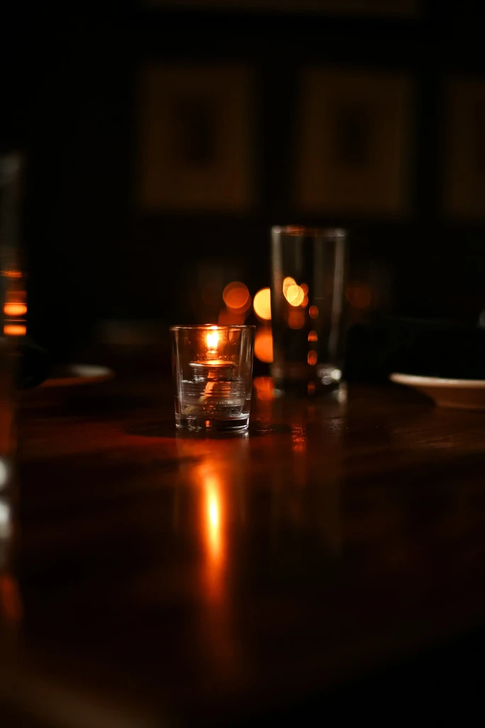 Burning candle casts warm glow on a reflective dark table.