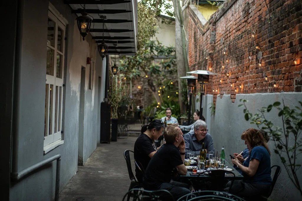 Outdoor dining patio with people, string lights, and brick and grey walls.