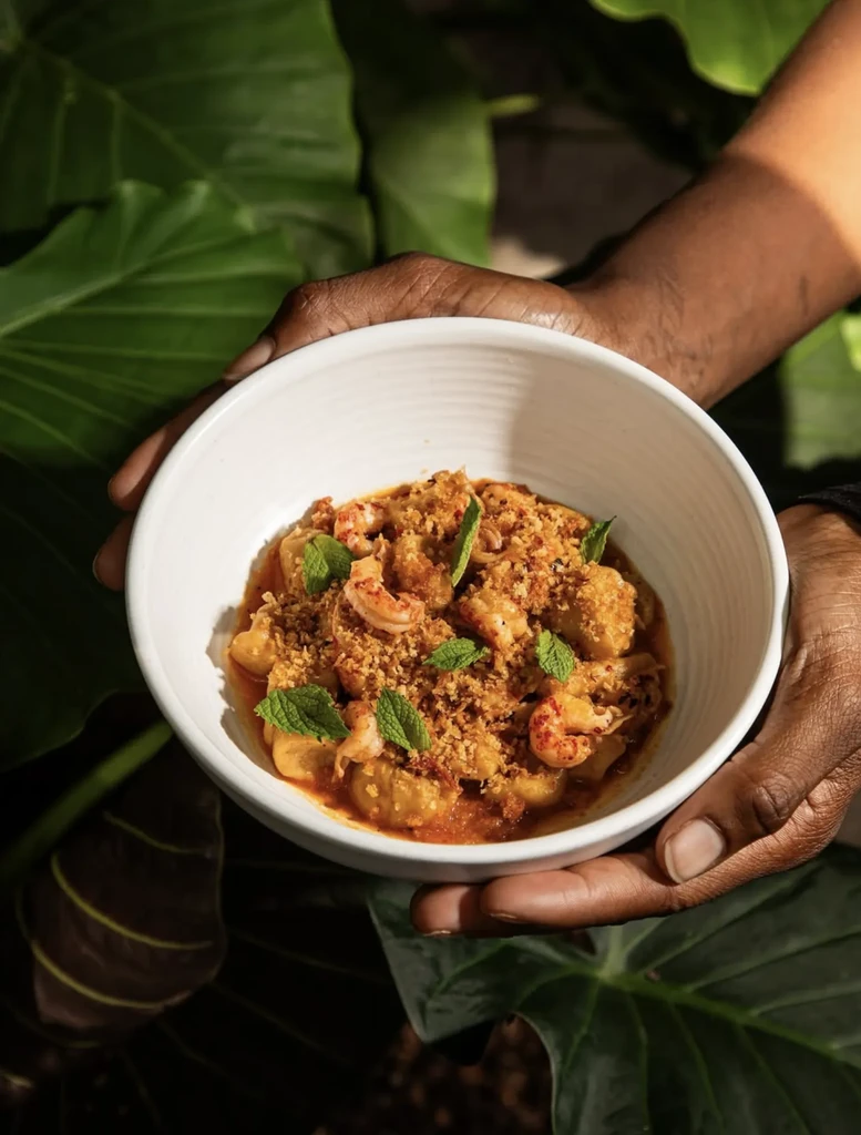 Hands hold gnocchi with shrimp in red sauce, mint, tropical background.