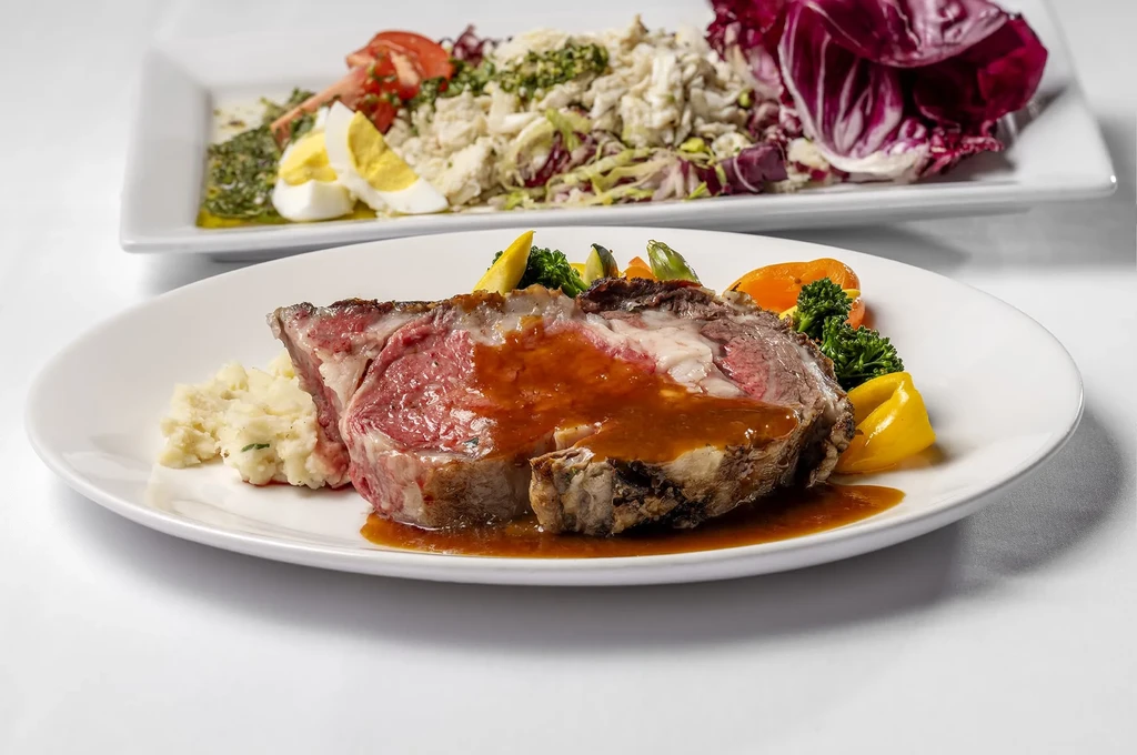Medium-rare roast beef with gravy, mashed potatoes, and colorful vegetables.