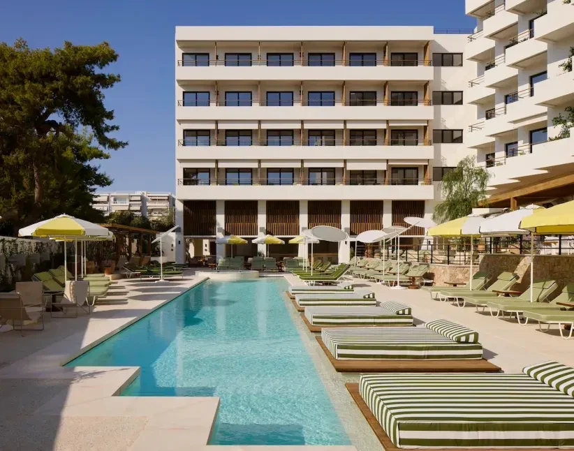 Sunny resort pool, striped daybeds, umbrellas, and modern building. No people.