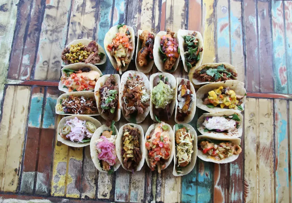 Overhead view of varied tacos on a rustic, colorful wooden table.