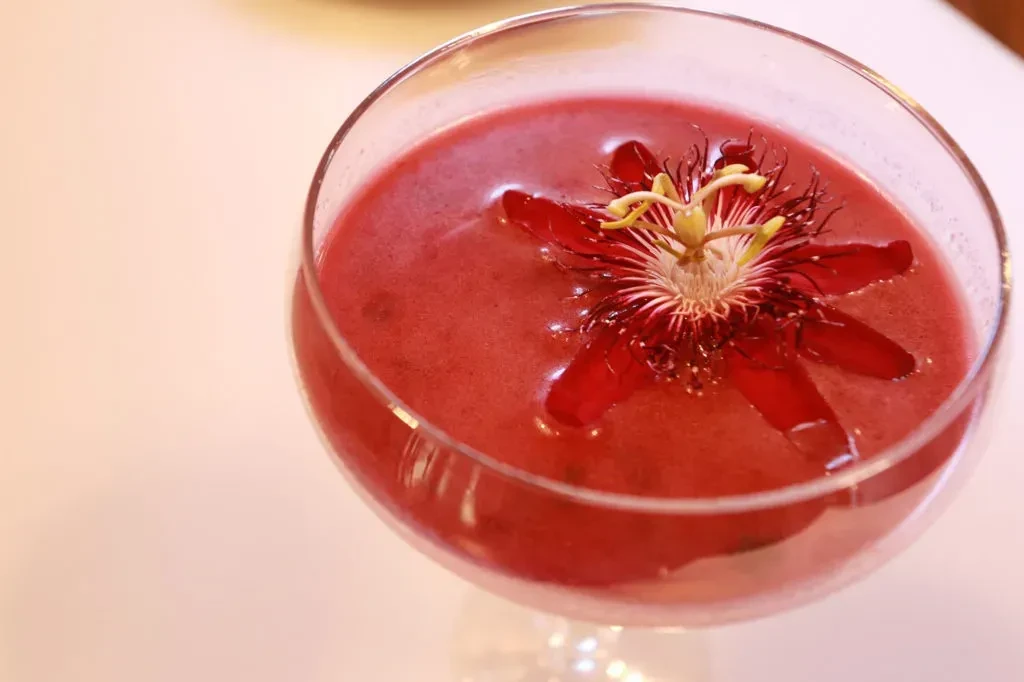 Pink drink in a stemmed glass with a red passionflower garnish.