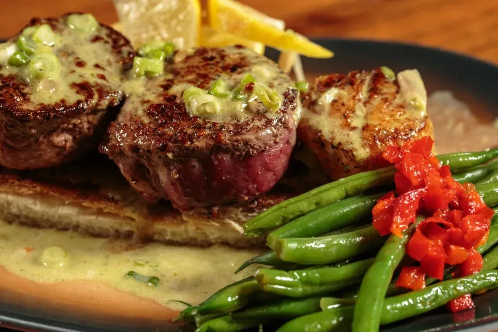 Seared beef medallions with green sauce, string beans, and red bell peppers.