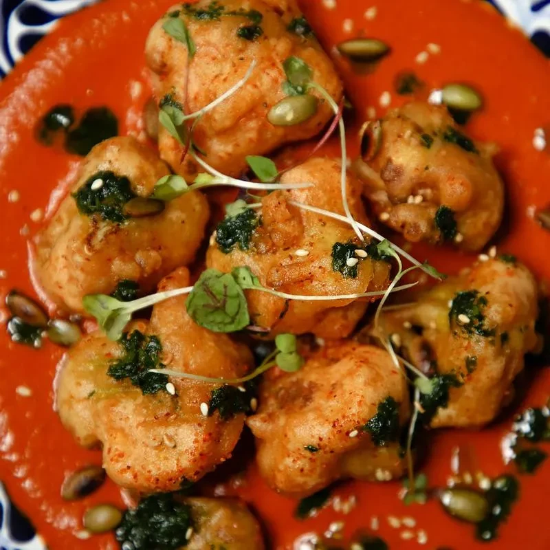 Golden fried fritters on red sauce, garnished with herbs and seeds.