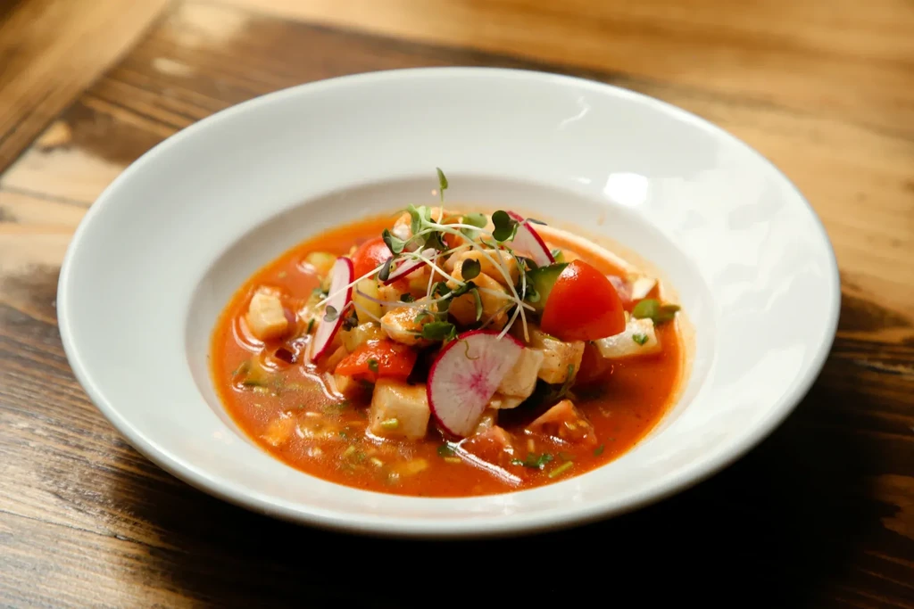Top-down vibrant seafood dish with fish, tomatoes, radishes, and microgreens.