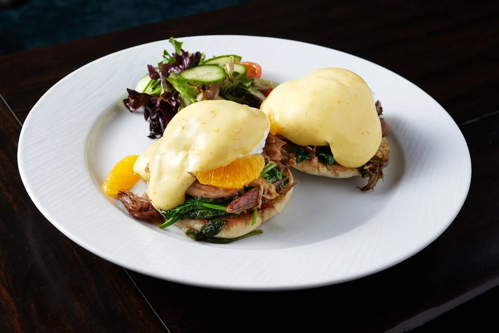 Gourmet Eggs Benedict with pulled meat and a fresh side salad.