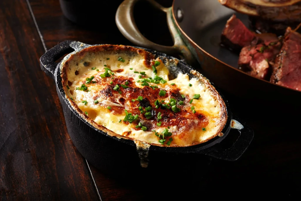 Bubbly golden-brown gratin, garnished with chives, in an oval cast iron dish.