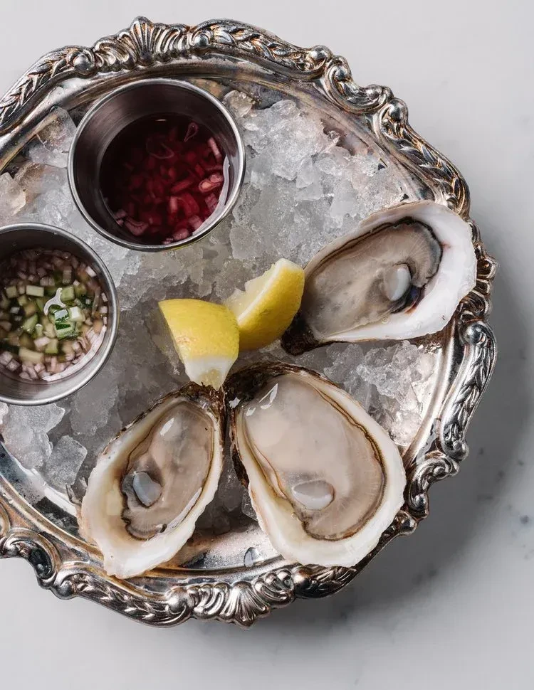 Three shucked oysters on ice with lemon wedges and two sauces.