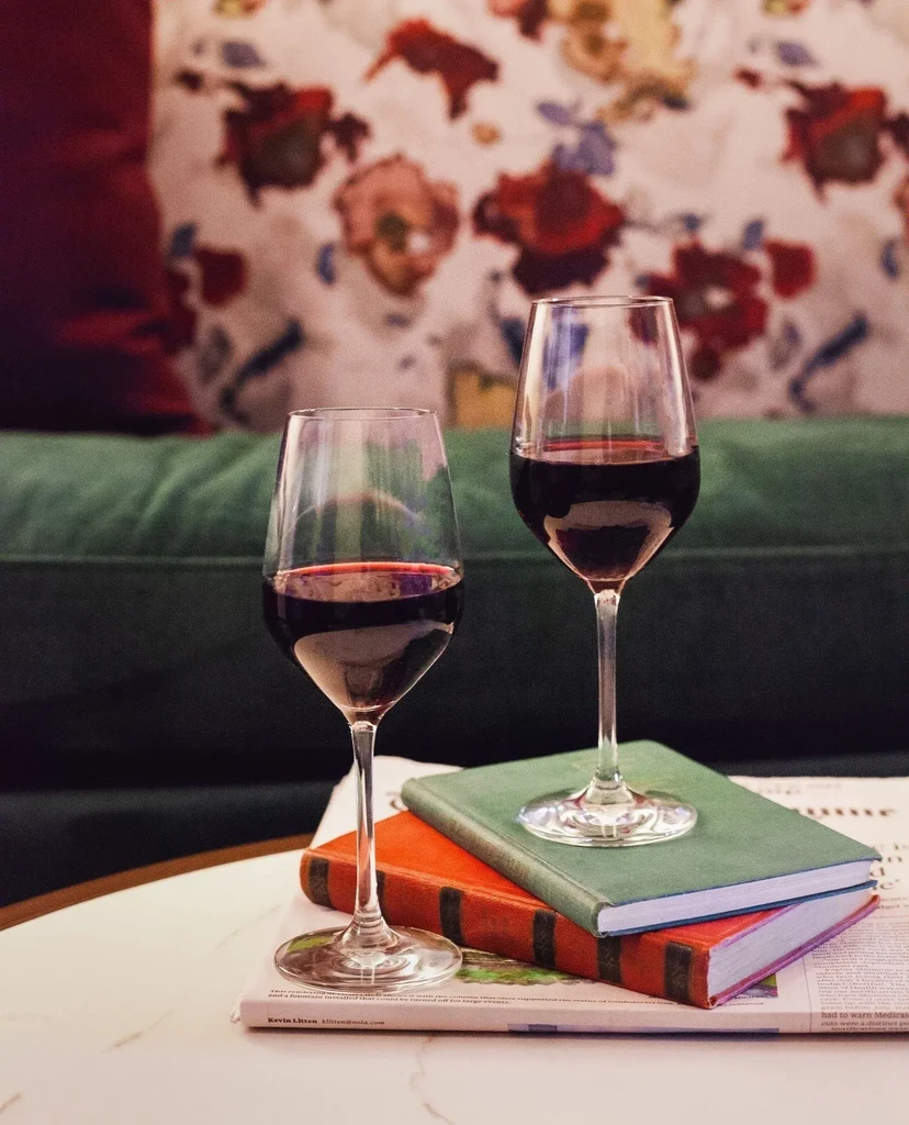 Two red wine glasses, stemmed and stemless, on books and magazine.