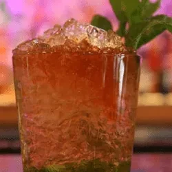 Colorful, layered cocktail with crushed ice and mint in textured glass.