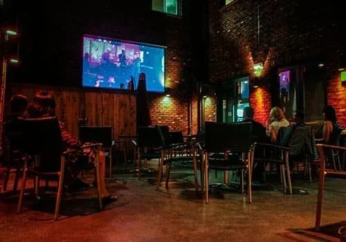 Warmly lit bar patio at night with a concert playing on screen.
