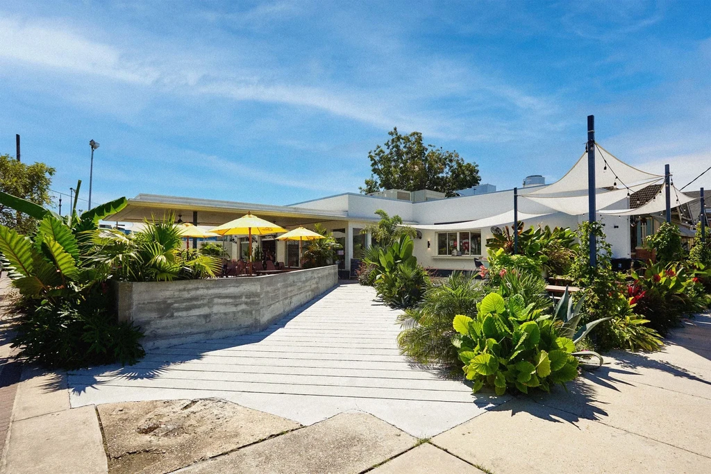 Modern white restaurant exterior with outdoor dining and tropical plants.