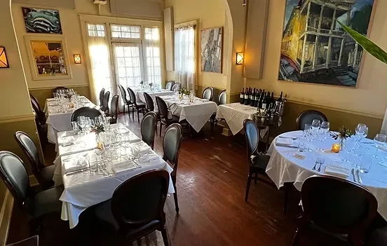 Empty, elegant dining room with set tables, dark floor, sunlit.