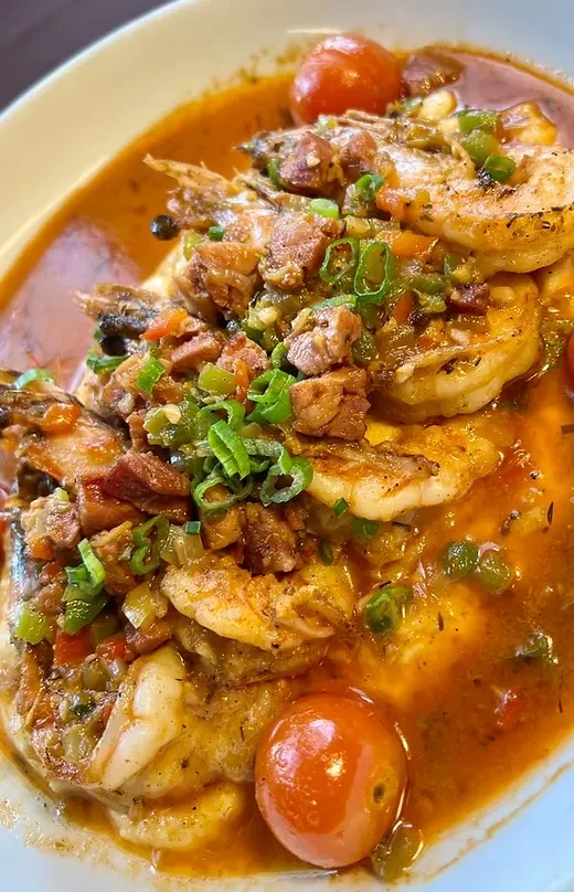 Close-up shrimp and grits in reddish sauce, garnished with vegetables and tomatoes.