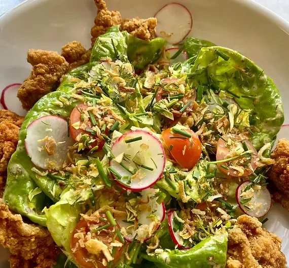 Green leaf lettuce salad with radishes, tomatoes, fried shallots, and fried chicken.