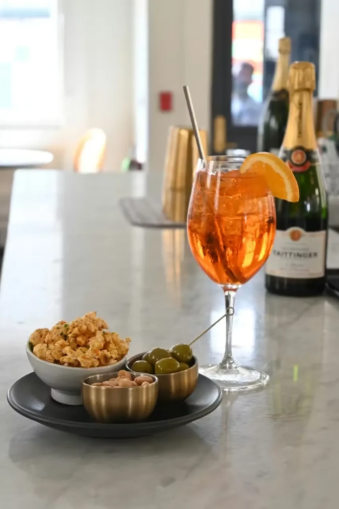 Aperol Spritz, appetizers, and champagne bottles on a bar counter.