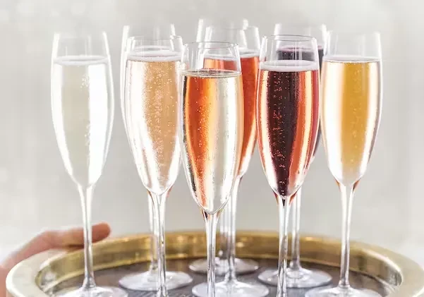 Hand carrying a golden tray with eight assorted sparkling wine flutes.